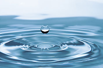 A single water droplet falling into still water, forming concentric rings